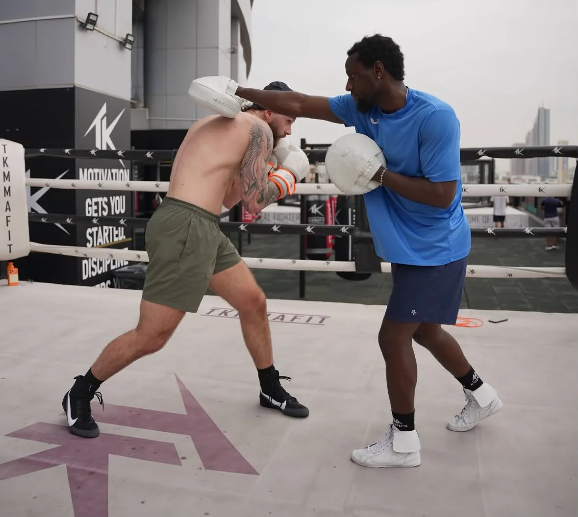Coach Allid, a boxing coach in Dubai, holding pads for a boxer in an outdoor ring